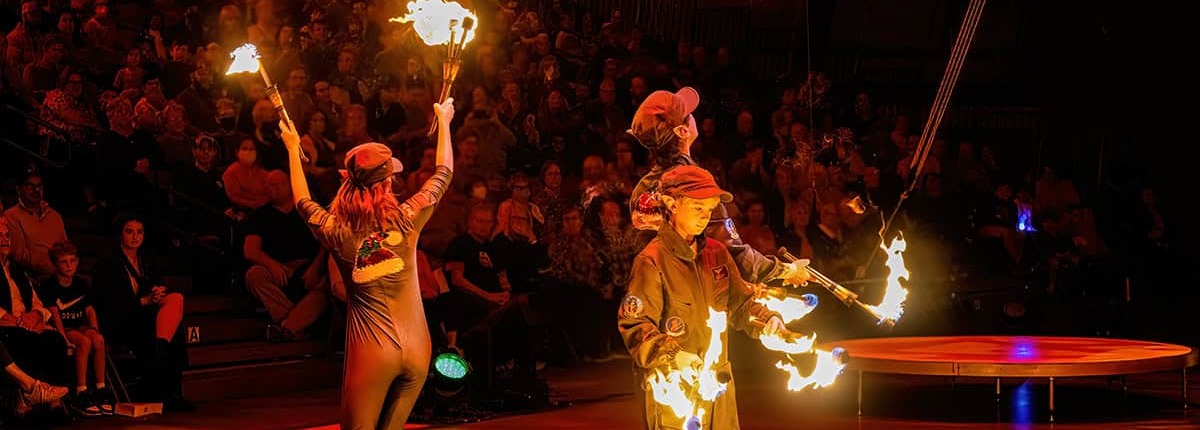 Flame performers shape fire on stage during a circus show, captivating the audience with fire dancing and aerial acts.
