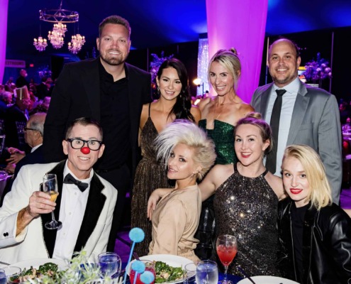 Clown with guests at circus staging event, vibrant party atmosphere with elegant attire and festive decorations.