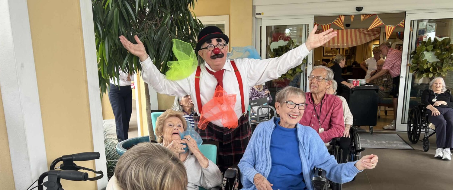 Slider1 Clown entertaining elderly residents at a senior care facility with lively circus staging and colorful decorations.