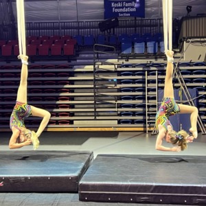 Flexible circus performers on aerial silk in a circus staging environment.