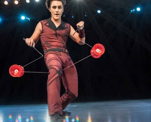 Juggler performing on a stage with bright lights and colorful reflections, showcasing circus arts and stage performance skills.
