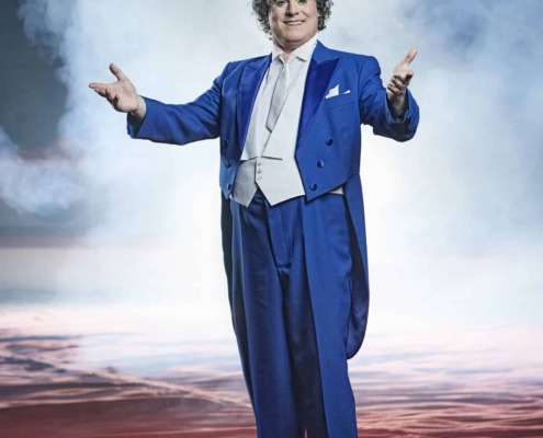 Vibrant circus performer in blue tuxedo on stage with dramatic smoky background, showcasing circus staging and performance art.