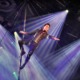 Acrobat on aerial pole performing circus arts staging under vibrant stage lighting.