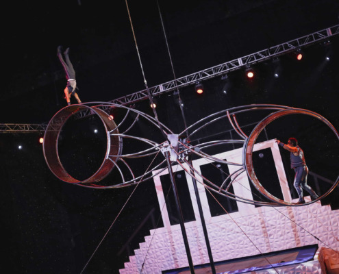 Aerial performance on circus staging with acrobats and metabolic rings, illuminated stage with lighting effects.