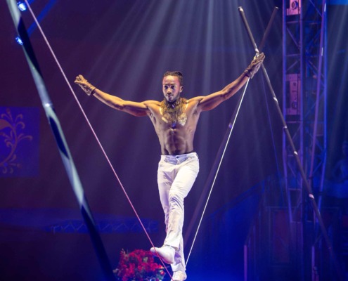 Balancing performer on tightrope at circus staging during acrobatic show.