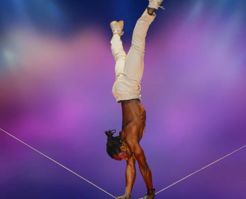 Flexible acrobat performing handstand on tightrope at circus staging event.