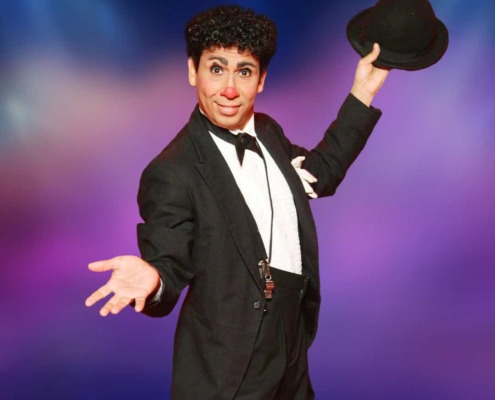 Clown holding a black hat on a colorful circus stage for entertainment and circus staging photos.