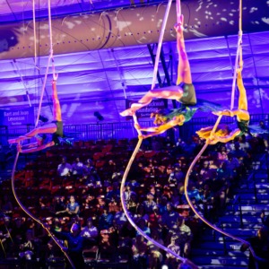 Aerial acrobats performing on circus stage rigging for a live audience.