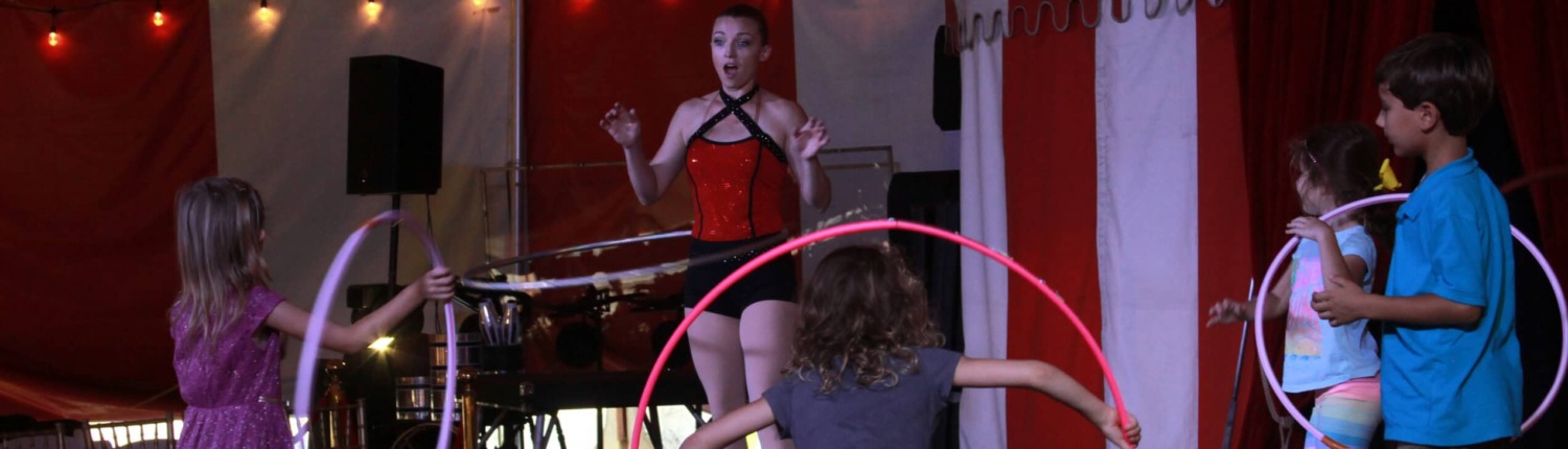 banner Colorful circus stage with kids and performer engaging in hula hoop act at circus arts event.