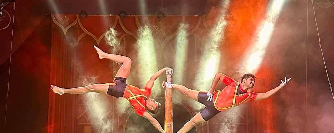 High-quality circus staging with acrobats performing balancing acts on a pole under vibrant stage lighting.