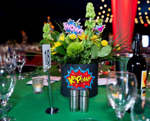 Vibrant flower centerpiece with comic book style "WOW" and "KAPOW" graphics, perfect for circus-themed staging.