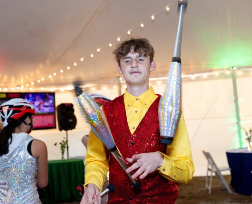 Bright young juggler performing circus stunts at an indoor event with colorful lighting and audience.